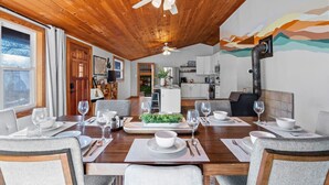 Een eetgedeelte met een houten plafond, uitzicht op de keuken, en een gedekte eettafel voor zes personen.