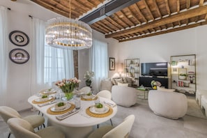 A dining area with a round table set for four, a chandelier, and a modern living room with a sofa and TV. - The Joia House in Lucca (Lucca)