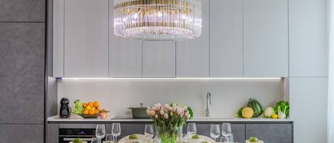 A modern kitchen with a dining table set for six, a chandelier, and a fruit bowl on the counter.