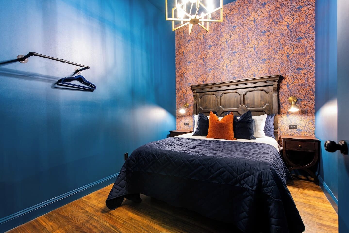 Ein Schlafzimmer mit einem großen Bett, einem Holz-Kopfteil und einer blauen Wand mit Baum-Motiv.