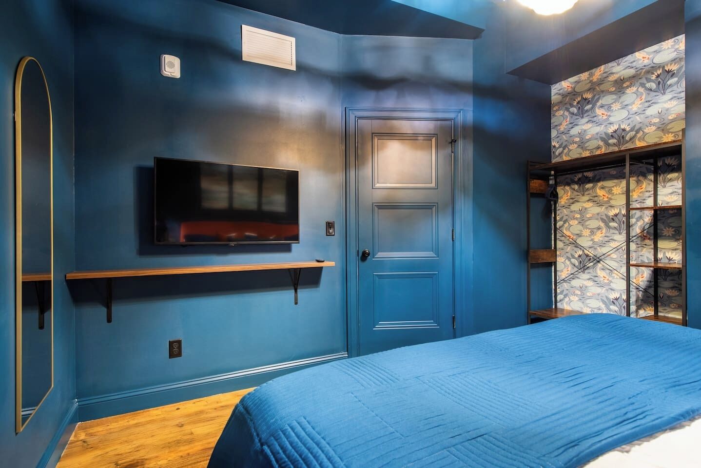 Een slaapkamer met een blauwe muur, een wandtelevisie, een deur en een raam met een decoratief gordijn.