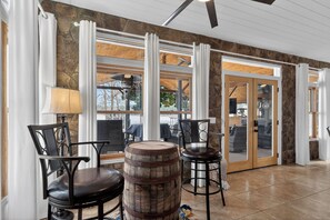 A room with stone walls, large windows, and a wooden ceiling. There are two chairs and a wooden barrel. - The 127 at Lake Sinclair: Sleeps 16, Prime Location, Amazing Outdoor Space!! (Milledgeville)