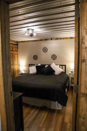 Un dormitorio con cama, lámparas de noche, una puerta de madera y una lámpara en el techo.