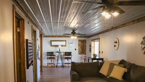 A room with a wooden ceiling, a sofa, a coffee table, and a dining area with chairs and a table. - Lakeview LaFollette Retreat, Sleeps 10 - Game Room (LaFollette)