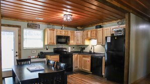 A kitchen with wooden cabinets, a black refrigerator, a microwave, and a dining table with chairs. - Lakeview LaFollette Retreat, Sleeps 10 - Game Room (LaFollette)