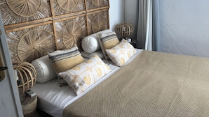 A bed with a woven headboard, multiple pillows, a bedside lamp, and a window with curtains. - Villasimius vacation home with private pool spectacular sea view golf porto (Villasimius)