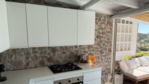 A kitchen with white cabinets, a gas stove, and an oven. There is a stone wall behind the cabinets and a view of the outdoors through a window. - Villasimius vacation home with private pool spectacular sea view golf porto (Villasimius)