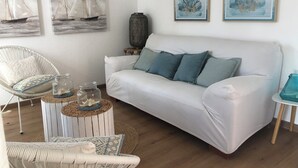 A living room with a white sofa, a wicker chair, a round coffee table, and two paintings of sailboats and coral. - Villasimius vacation home with private pool spectacular sea view golf porto (Villasimius)