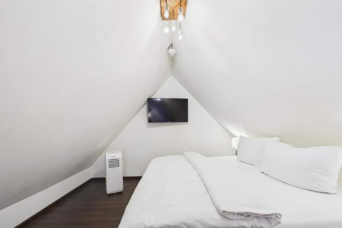 A bedroom with a bed, a flat-screen TV mounted on the wall, and a white air conditioning unit.