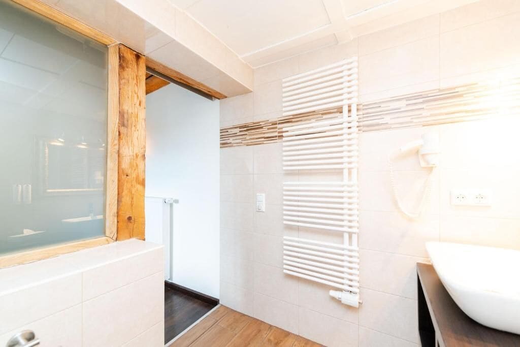 A modern bathroom with a glass shower enclosure, a wooden beam, a white radiator, and a white sink.
