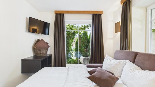 Ein Hotelzimmer mit einem Bett, einem Fernseher, einem Fenster mit Vorhängen und Blick auf Grünfläche.