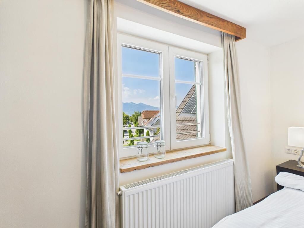 A hotel room with a large window, a wooden beam above it, and a white radiator below.