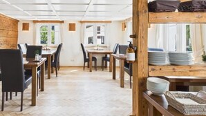 Ein Essbereich mit Holztischen und -stühlen, ein Etagenbett mit Matratze und Kissen sowie ein Fenster mit Vorhängen.