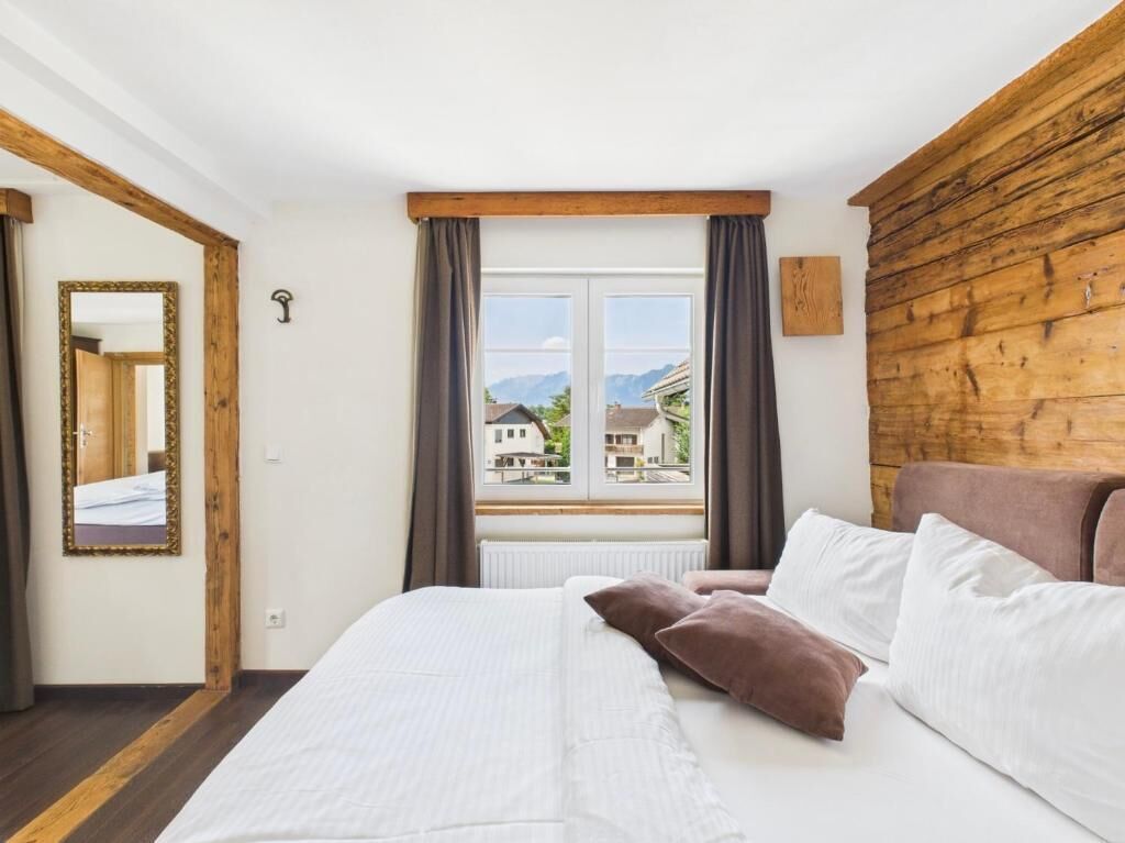 A bedroom with a bed, a window with curtains, a wooden headboard, and a mirror on the wall.