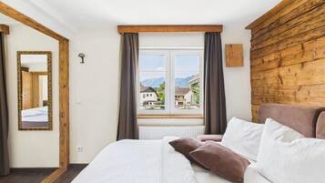 A bedroom with a bed, a window with curtains, a wooden headboard, and a mirror on the wall.