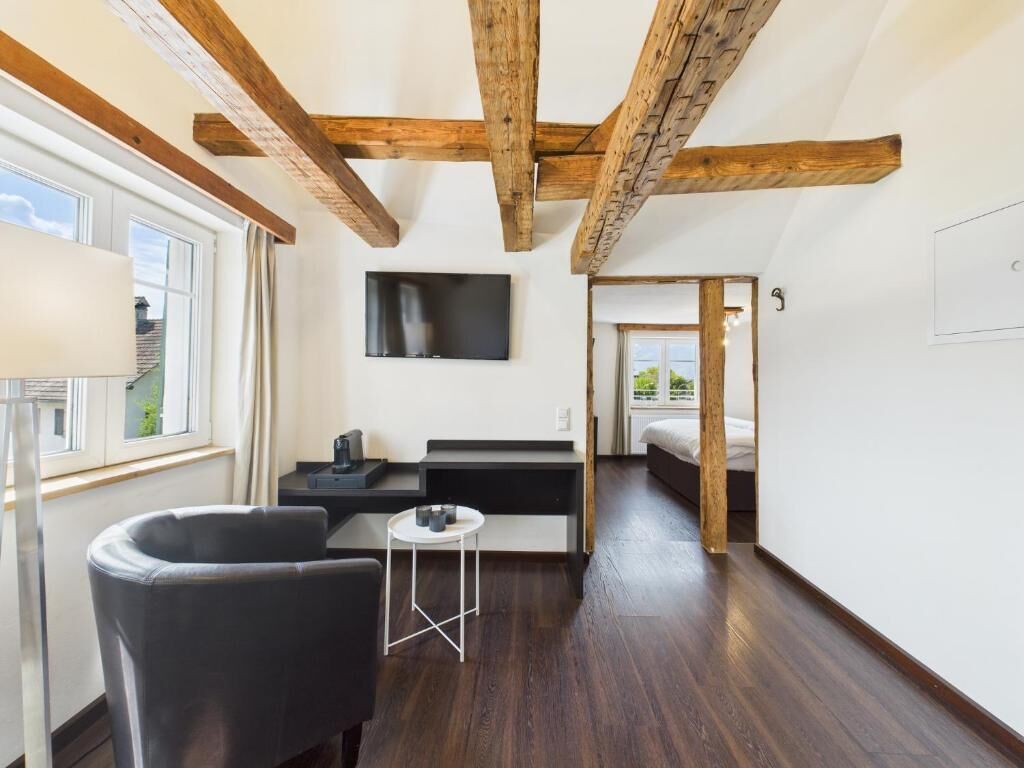 Ein modernes Zimmer mit freiliegenden Holzbalken, einem Flachbildfernseher, einem Schlafsofa, einem kleinen Tisch und einem Bett.