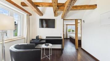 Ein modernes Zimmer mit freiliegenden Holzbalken, einem Flachbildfernseher, einem Schlafsofa, einem kleinen Tisch und einem Bett.