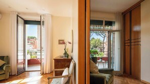 Un'ampia zona giorno con pavimento in legno, un divano, una poltrona, un tavolino e un balcone con vista sulla città.