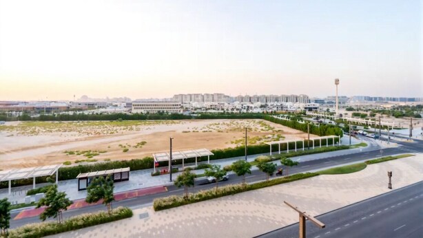 A modern urban landscape with a wide road, green spaces, and distant buildings. - Vogue | The Gate near Yas Island | Ferrari World (Abu Dhabi)