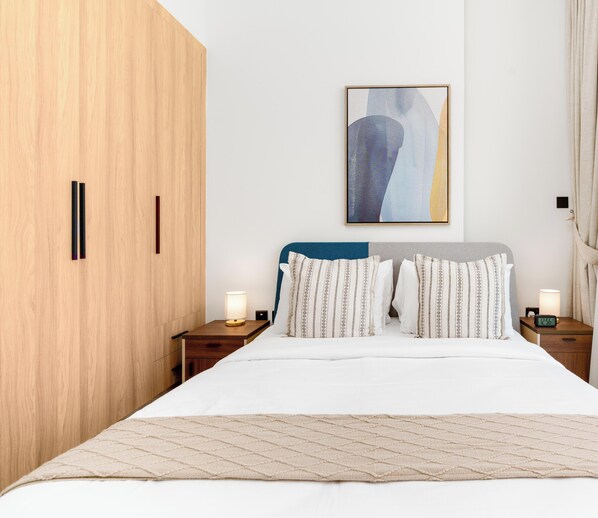 A neatly arranged bedroom with a bed, two bedside tables with lamps, a wooden wardrobe, and a framed abstract painting on the wall. - Vogue | The Gate near Yas Island | Ferrari World (Abu Dhabi)