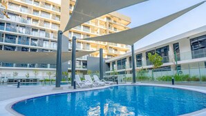 Una piscina con sillas de descanso, rodeada de edificios modernos con balcones.