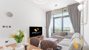 Una sala de estar moderna con sofá, comedor, televisor y un amplio ventanal con cortinas.