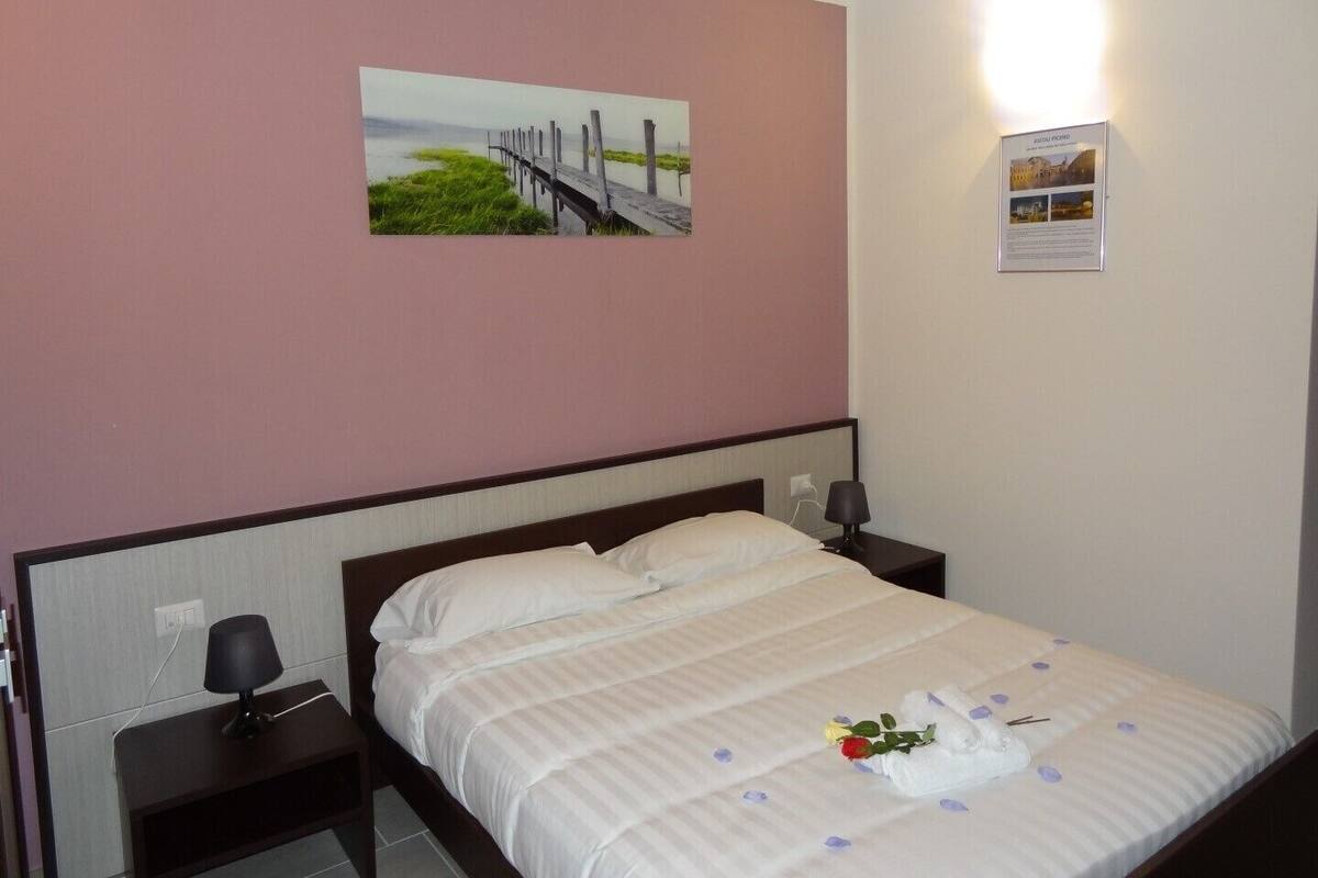 A hotel room with a bed, a nightstand, a lamp, a picture on the wall, and a sign.