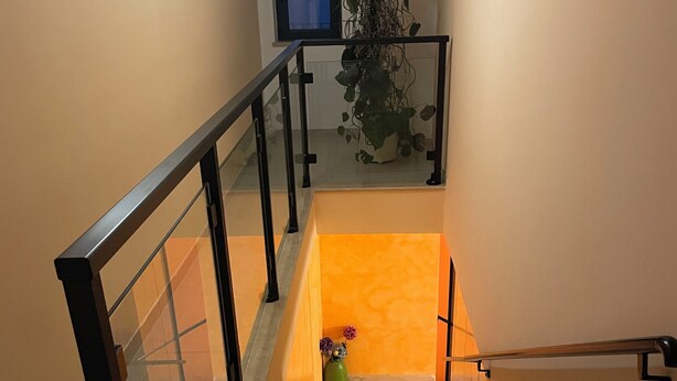 A staircase with a glass railing, a plant, and a window in the background. - ROOMS DI MATTEO (San Paolo di Jesi)
