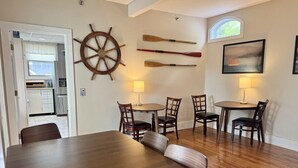 A dining area with a large wooden table, four chairs, a ship's wheel, and several paddles on the wall.