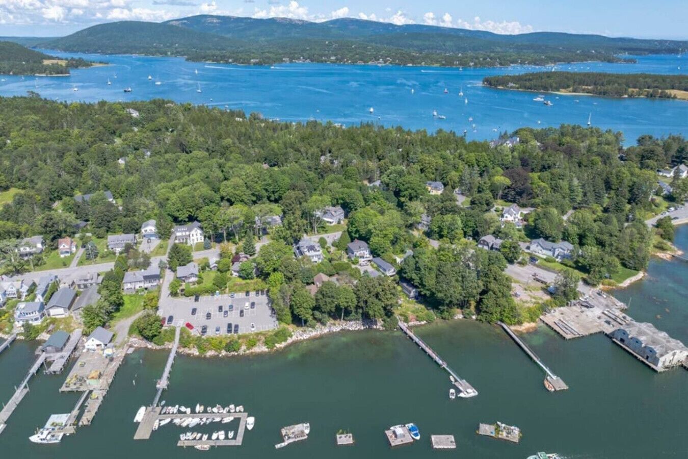 An aerial view of a coastal residential area with houses, a marina, and a large body of water.