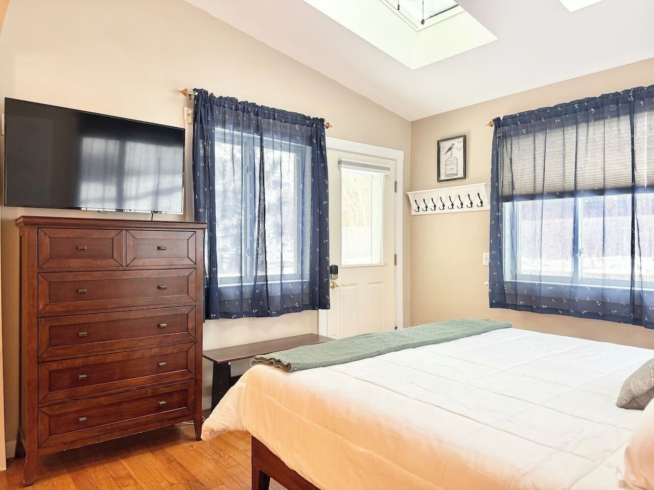 A bedroom with a bed, a dresser, a TV, and two windows with curtains.