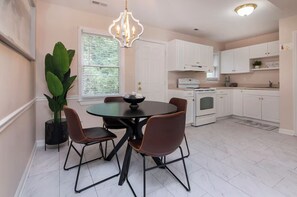 A modern kitchen with white cabinets, a dining table with four chairs, a chandelier, and a potted plant. - Comfort-Ready 2BR for Work Trips (Charlotte)