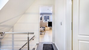 Ein Flur, der zu einer Küche mit Essbereich, einer Treppe mit Handlauf und einer Tür rechts führt.