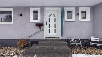 Ein Haus mit weißer Tür, einem Briefkasten und einer kleinen Sitzgelegenheit mit zwei Stühlen.