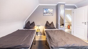 Eine kleine, einfache Unterkunft mit zwei Einzelbetten, einem Nachttisch mit Lampe, einem gerahmten Bild an der Wand und einer Tür zu einem Badezimmer.