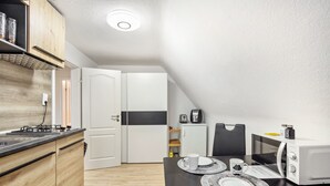 Eine kompakte Küche mit Herd, Mikrowelle und Kühlschrank. Ein Esstisch mit Tellern und einer Tasse.