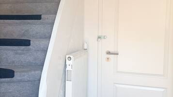 Un escalier avec une porte blanche en bas, un radiateur blanc et une petite plateforme recouverte d’une moquette noire.