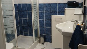 Ein Badezimmer mit Duschkabine aus Glas, einem weißen Waschbecken und blautonierten Fliesen.