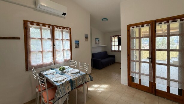 Un comedor con una mesa dispuesta para cuatro personas, un sofá y un gran ventanal corredizo que da al exterior.