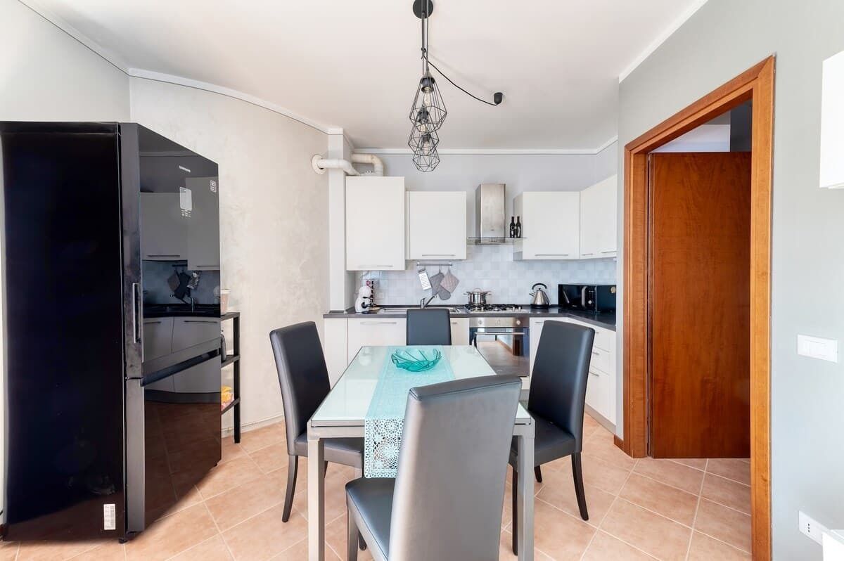 Una cocina compacta con armarios blancos, un refrigerador negro y un comedor con mesa y sillas.