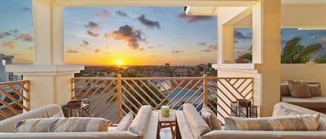 A rooftop terrace with a sunset view, wooden furniture, and a pool.