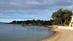 A sandy beach with footprints, a calm sea, and a coastal town in the background. - LA Péguière, 2-room apartment (27m²), for 2 adults and 1 child, air-conditioned, garden, parking and beach 5 minutes walk away (Saint Raphael)