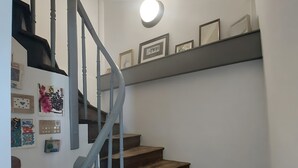 A staircase with wooden steps and a gray railing, leading to a landing with framed pictures and a round light fixture. - Holiday Home 'Bienvenue À La Maison' with Private Terrace, Garden & Wi-Fi (Mézos)