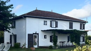 A white building with a tiled roof, a wooden fence, and pink flowers in the foreground. - Holiday Home 'Bienvenue À La Maison' with Private Terrace, Garden & Wi-Fi (Mézos)