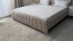 A modern bedroom with a large bed, a bedside table with a lamp, and a view through a window with curtains. - Charming apartment in fantastic Mombasa perfect for your getaway (Mombasa)
