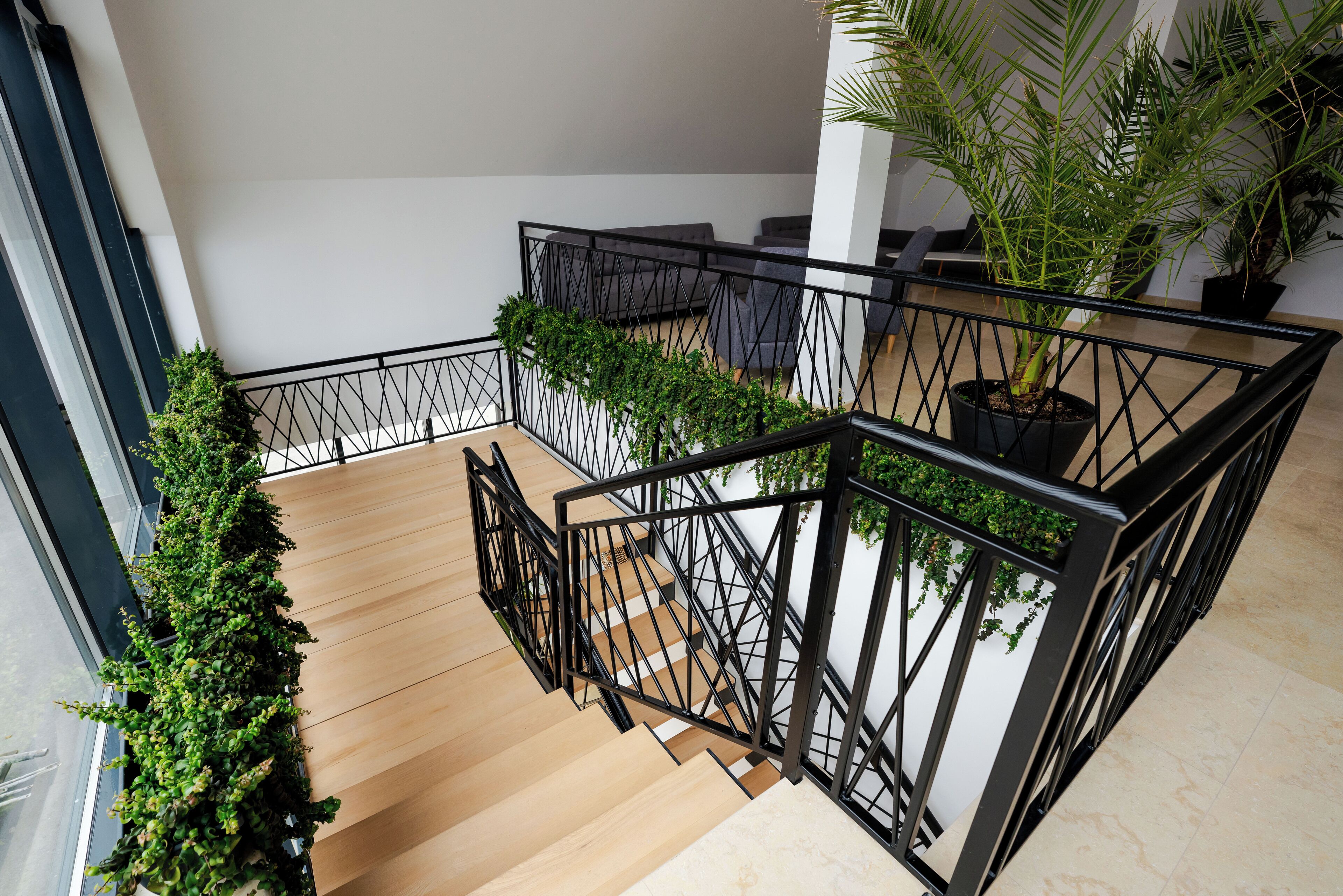 A modern staircase with wooden steps and black metal railings, surrounded by potted plants and a view of the interior space.