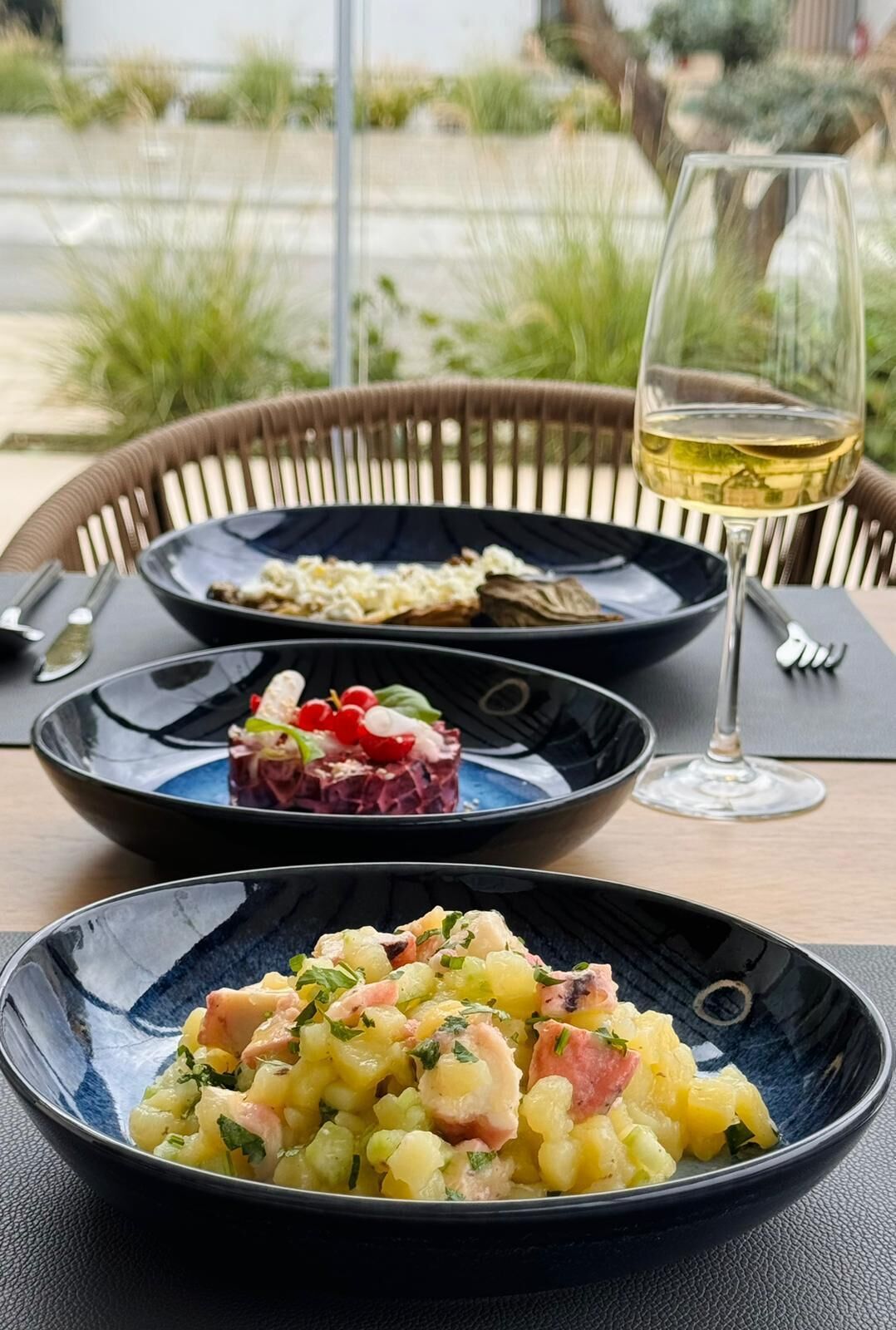 A dining table with three plates of food and a glass of wine.