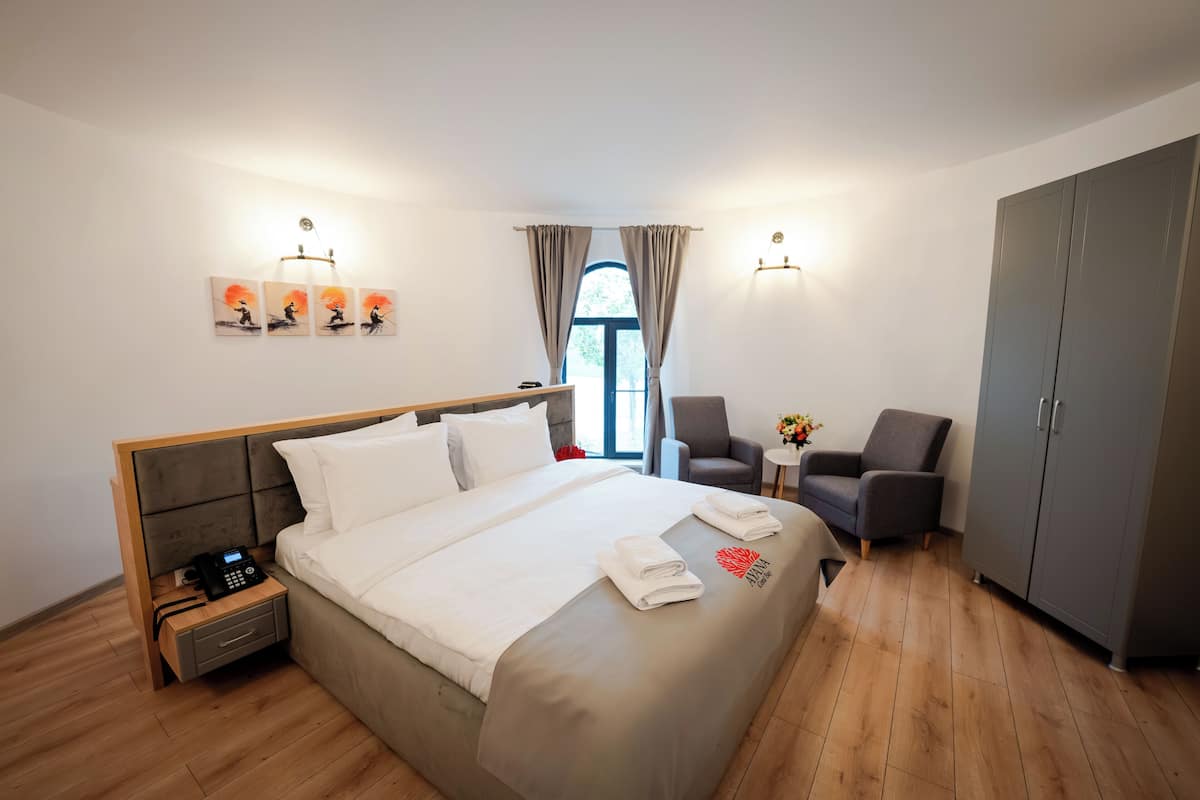 A hotel room with a bed, bedside table with a phone, two chairs, a small table with flowers, and a wardrobe.