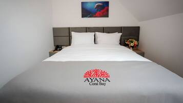 Habitación de hotel con una cama, una mesita de noche con un teléfono, un cuadro de delfín y un logo en la colcha.