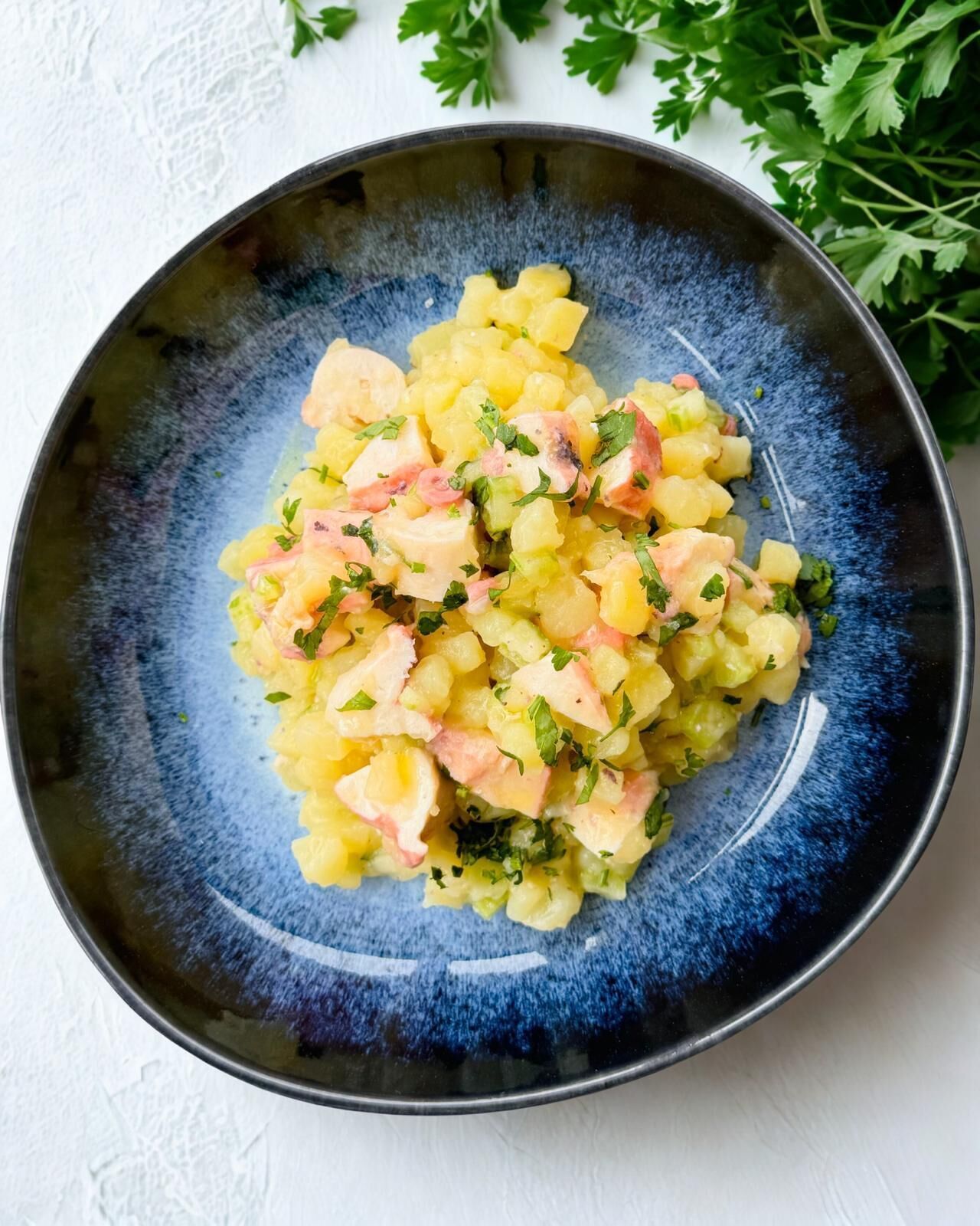 A bowl of potato salad with ham and parsley on a blue plate.